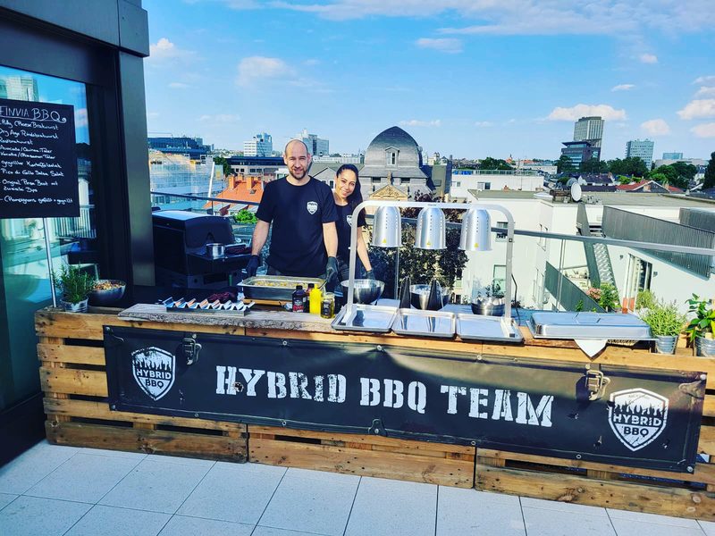 Hybrid BBQ Team hinter der Grillstation auf einer Dachterrasse über den Dächern von Frankfurt