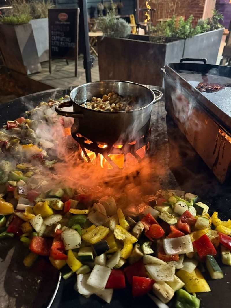 Feuerschale mit gegrilltem Gemüse und Schmortopf über offener Flamme bei einem Firmen-BBQ
