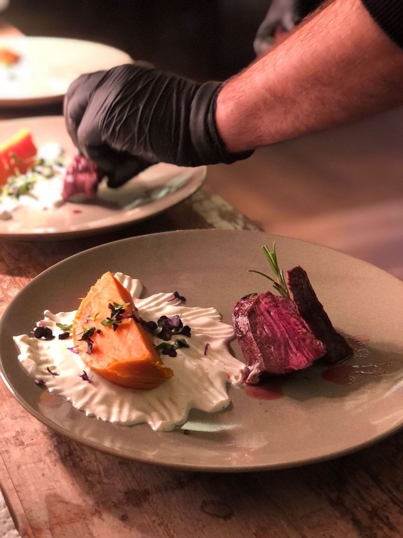 Angerichteter Teller mit rosa gegrilltem Rindfleisch, Süßkartoffel und Creme beim Live-Plating