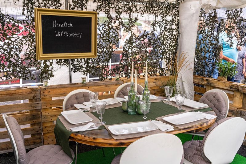 Festlich gedeckte Tafel im Garten mit Willkommenstafel und Kerzen für eine private Feier