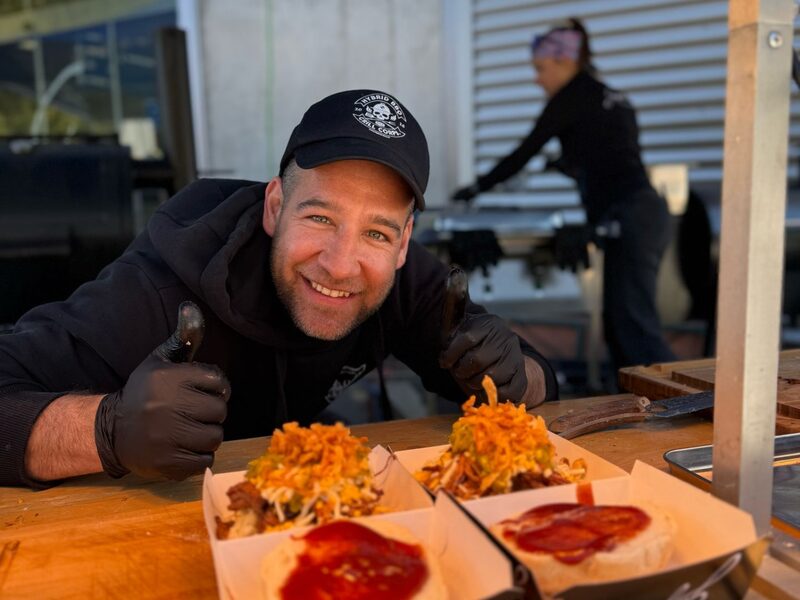 Michael Kisperth mit Daumen hoch hinter zwei angerichteten Pulled-Beef-Burgern